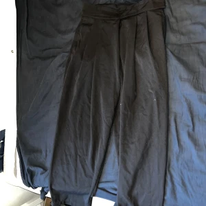 Svarta vida kostymbyxor med hög midja - Säljer ett par svarta kostymbyxor med hög midja och vida ben. Byxorna har pressveck framtill och två bakfickor. Snyggt skräddad look och passar perfekt till en stilren outfit.