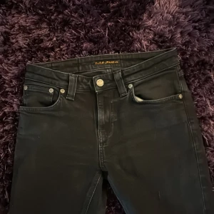 Svarta slim jeans från Nudie Jeans - Svarta skinny jeans från Nudie Jeans med klassisk femficksdesign och snygga detaljer på bakfickorna. Jeansen har smal passform, normal midja och är tillverkade i stretchig bomullsdenim för en bekväm känsla. Perfekta till sneakers eller boots.