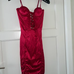 Röd satin klänning med snörning - Helt ny med prislapp från Oh Polly. Säljer en röd, figurnära klänning i satin med smala axelband och snygg snörning framtill. Klänningen har kupor och markerar midjan. Perfekt för dig som vill sticka ut med en elegant och sexig look.