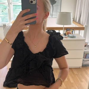 Svart omlott blus med volanger - Säljer en svart blus från Monki med omlott-design och volangdetaljer. Blusen är croppad, har korta ärmar och v-ringad hals. Materialet är tunt och lätt, perfekt för dig som gillar en luftig och trendig look.