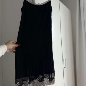 Svart kort klänning med spetsdetaljer - Säljer en svart kort klänning med tunna axelband och snygga spetsdetaljer i vitt vid halsringningen och nederkanten. Från Intimissimi, bra skick💕