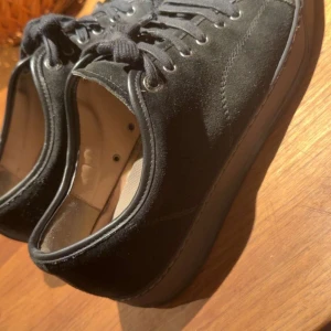 Svarta Lanvin - Snygga svarta sneakers från Lanvin Paris med mocka på sidorna och blank tå i skinn. Klassisk rund tå och platt sula, med svarta snören och metallöglor. Perfekt för dig som gillar stilrena och lyxiga detaljer i din outfit. Skorna är i bra skick och dustbag ingår.
