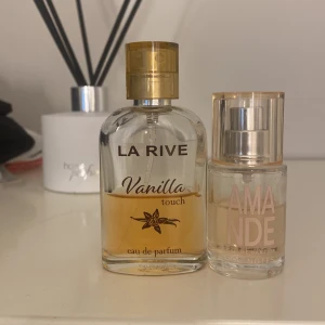 La Rive Vanilla Touch & Amande parfym - Två parfymer säljes: La Rive Vanilla Touch i genomskinlig glasflaska med guldlock och söt vaniljdoft, samt Amande från 50 Notes i mindre rund glasflaska med transparent lock och mjuk mandeldoft. Perfekta för dig som gillar varma, gourmandiga dofter.