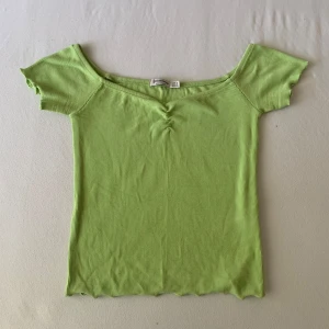 Ljusgrön ribbad topp från Stradivarius - Superfin ljusgrön topp från Stradivarius med ribbad struktur och offshoulder-modell. Toppen har korta ärmar, rynkdetalj framtill och vågig kant nertill för en extra söt touch. Perfekt för dig som gillar färg och vill sticka ut lite extra.