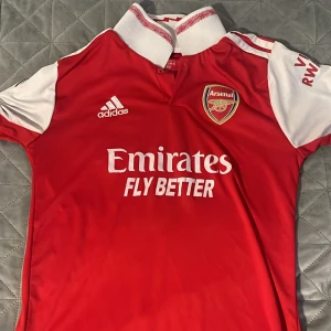 Arsenal fotbollströja - Detta är en super snygg Arsenal tröja som knappast har använts. Den har storlek S men borde passa perfekt även till M ifall man vill visa musklerna. Säljer den för 350 kr eftersom den endå inte är använt så länge och så har den inga skador. Äkta 100%.