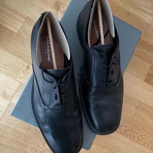 Vagabond Andrew kostymskor/skinnskor - Klassiska svarta skinnskor från Vagabond med rund tå och snörning. Snygg minimalistisk design med platt sula och diskreta sömmar. Vagabond Andrew svarta kostymskor i gott skick. Bara använda ca 6-7 gånger och storlek 43. Testade en ny snörning senast men går hur bra som helst att byta tillbaka till vanlig snörning såklart. Nypris 1700.