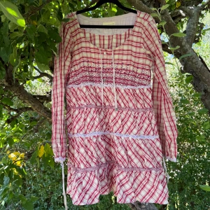 Odd Molly rutig kortklänning med snörning - Superfin kortklänning/ tunika från Odd Molly i röd- och vitrutigt mönster. Klänningen har långa ärmar med snörning vid ärmslut, dekorativa broderier och knytband vid halsen. Tillverkad i mjuk bomull, perfekt för dig som gillar boho-vibe och detaljer. Storlek 3 som enligt deras storleksguide motsvarar en storlek L.  Fint skick, men den är tyvärr något missfärgat och den beige färgen är strakare i verkligen. Banden har några lösa trådar och kan vara något missfärgat. 