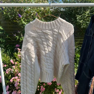 Vit stickad tröja från Monki - Säljer en chunky vit stickad tröja från Monki i storlek S. Tröjan har grova flätstickade detaljer, ribbad hög hals och långa ärmar. Perfekt och snyggt till hösten och vintern.