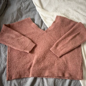 Rosa stickad v-ringad tröja - Mysig stickad tröja i en mjuk rosa ton med v-ringad hals och långa ärmar. Ribbad struktur ger en skön och avslappnad känsla. Perfekt att slänga på sig när det är lite kyligt ute. Passar dig som gillar enkel och stilren design.