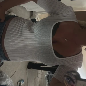 Vit ribbad topp med fyrkantig ringning - Säljer en vit ribbad topp med snygg fyrkantig ringning och korta ärmar. Toppen är figurnära och har en modern, croppad känsla som passar perfekt till jeans eller kjol. Enkel men ändå trendig design som lyfter din outfit.