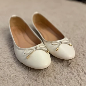Vita ballerinaskor - Snygga vita ballerinaskor från Day-Vine med rund tå och dekorativ rosett framtill. Skorna har guldfärgade detaljer på rosetterna och en mjuk innersula för extra komfort. Lite skavanker så pris går att diskutera.✨✨