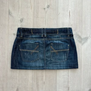Blå lågmidjad jeanskjol  - Mörkblå lågmidjad jeanskjol från Tom Tailor i storlek 38. Tvärs över midjan är det 40 cm och den är 29 cm lång (längs med sidan). Fint skick. Använd gärna köp nu!