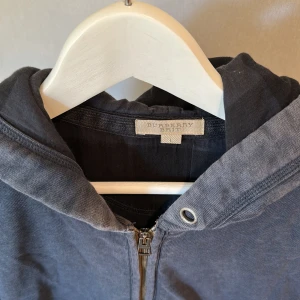 Mörkblå hoodie från Burberry Brit - Snygg mörkblå hoodie från Burberry Brit med dragkedja framtill och två stora fickor. Tröjan har huva med kontrastkant och är tillverkad i mjuk bomull. 