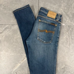 Blå  jeans från Nudie Jeans - Snygga blå jeans från Nudie Jeans med klassisk orange söm på bakfickorna. De har en mörk tvätt som ger en cool vibe. Ställ gärna frågor vid minsta fundering 