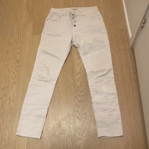 Vita jeansbyxor från Place du Jour - Säljer ett par vita jeansbyxor från Place du Jour med klassisk femficksdesign och en liten stjärndetalj på bakfickan. Byxorna har normal passform och är tillverkade i bomull med lite stretch för extra komfort.