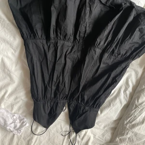 Svart klänning med dragsko från Zara - Säljer en svart klänning från Zara med dragsko i midjan och nertill. Klänningen har en lös passform och är tillverkad i ett lätt material, perfekt för varmare dagar. Enkel och stilren design som passar till många tillfällen.