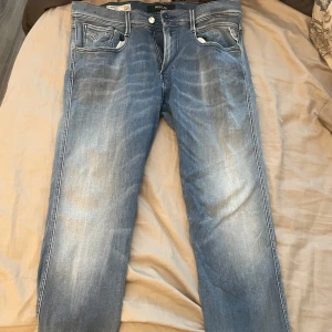 Replay Anbass ljusblå jeans - Säljer ett par Replay Anbass jeans i ljusblå tvätt med klassiska fem fickor och snygga slitningar. Jeansen har normal passform och raka ben, perfekt för en avslappnad stil. Stängs med dragkedja och knapp.helt nya 