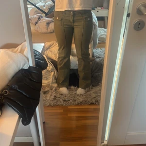 Olivgröna byxor med fickdetaljer - Säljer ett par olivgröna byxor snygga fickor framtill med knappar. Byxorna har normal passform och är tillverkade i ett bomullsliknande material. Perfekta för dig som vill ha en stilren och enkel look. Dem är insydda