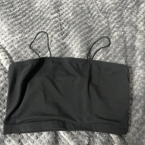 Svart tubtopp med smala axelband från SHEIN - En enkel svart tubtopp från SHEIN med smala axelband. Toppen är ärmlös och har en minimalistisk design, perfekt att matcha med olika outfits. Tillverkad i ett mjukt och stretchigt material för en bekväm passform.