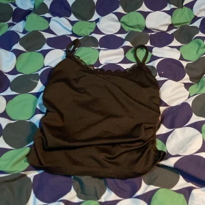 Svart linnetopp med spets från SHEIN - Säljer en svart linnetopp från SHEIN med tunna axelband och spetsdetalj längs urringningen. Perfekt att styla till olika outfits och enkel att matcha med andra plagg.