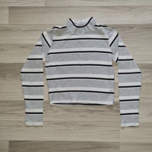 Randig Y2K polotröja från Bik Bok - Säljer en ribbad Y2K polotröja från Bik Bok i storlek S. Tröjan är vit med gråa och svarta horisontella ränder, har lång ärm och croppad passform. Perfekt för en stilren och trendig look.