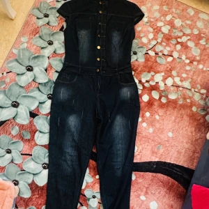 Tunn jeans-jumpsuit för dam – storlek S/M - Snygg och lätt jumpsuit i tunn denim med guldknappar och kort ärm. Perfekt för vår och sommar. Använd endast en gång – i nyskick. Passar storlek S till M. 