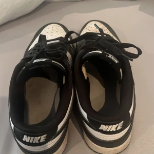 Nike Dunk Low svartvita sneakers - Säljer ett par klassiska Nike Dunk Low sneakers i svart och vitt. Skorna har snörning, rund tå och platt sula. Perfekta för dig som gillar streetwear och vill ha en stilren look med ikonisk Nike-logga på hälen.