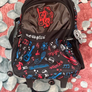 Scoobies rullväska/ryggsäck – musiktema – helt ny - Supercool och praktisk ryggsäck från Scoobies med musiktema och färgstark design. Med teleskophandtag och hjul – kan användas både som rullväska och ryggsäck. Mycket rymlig med flera fack och sidoficka för vattenflaska. Helt ny och oanvänd. Perfekt för skolan eller resor.