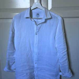 Vit linneskjorta från Zara - Säljer en klassisk vit skjorta från Zara i svalt linne. Skjortan har lång ärm, knappar framtill och en stilren krage. Perfekt för varma dagar eller när du vill ha en clean look. Hör av er vid intresse/ frågor!