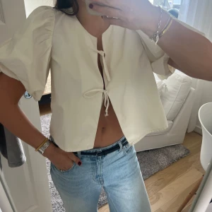 Vit blus med puffärmar och knyt - Säljer en söt vit blus med puffiga korta ärmar och två knyt framtill. Blusen har en luftig passform och är perfekt för vår och sommar. Enkel att styla till både jeans och kjol.