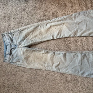 Lågmidjade jeans - Säljer ett par ljusblåa jeans som är lågmidjade och bootcut. Klassisk femficksmodell med dragkedja och knapp framtill. Perfekta för dig som gillar en smalare siluett och stilren look.