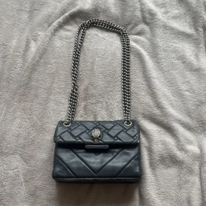 Svart väska från Kurt Geiger - Säljer en svart axelväska från Kurt Geiger med silverfärgad kedja och ikonisk örndetalj på locket. Väskan har magnetlås och är tillverkad i skinn. Perfekt för dig som vill ha en stilren accessoar med edgy känsla.