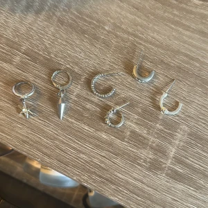 Set med sex silverfärgade örhängen - Säljer ett set med sex olika silverfärgade örhängen. Innehåller bland annat hoops med stjärna, konformad berlock, små stenar och minimalistiska bågar. Perfekt för att mixa och matcha flera hål i öronen. Säljes enskilda då jag har två hål på ett öra 29 för alla, 10 är ett.