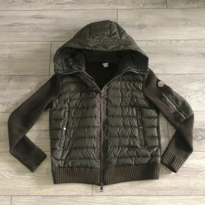 Moncler cardigan  - Snygg oliv grön cardigan från Moncler med quiltad front och huva. Jackan har stickade ärmar och rygg, dragkedja framtill och ribbade muddar. Perfekt för lager-på-lager och streetstyle. Den har små slitningar som knappt syns och lappen innuti är lös. Skriv för fler bilder! INGA BYTEN.