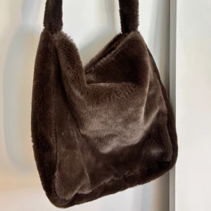 Mörkbrun fluffig axelväska - Supermjuk och fluffig mörkbrun axelväska med bred axelrem ⭐️ Väskan är rymlig och har ett stilrent, fyrkantigt snitt, min MacBook får även plats i den 🤩 Endast använd max 2 gånger, så i mycket bra skick!