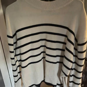 Vit och svart randig stickad tröja från Gina - Säljer en vit stickad tröja med svarta horisontella ränder. Tröjan har rund halsringning och långa ärmar. Perfekt för en avslappnad och stilren look. Tröjan är i storlek xs och kommer ifrån Gina.
