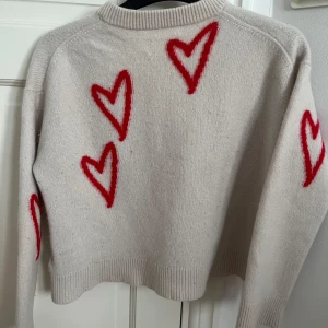 Beige stickad tröja med röda hjärtan från Zadig & Voltaire - Superfin beige stickad tröja från Zadig & Voltaire med röda hjärtan över hela tröjan. Tröjan har rund halsringning, långa ärmar och en croppad passform. Perfekt för dig som vill ha något gulligt och trendigt! Är storlek xs men sitter som xxs 