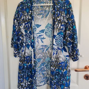 Blåvit mönstrad kimono från Steps - Säljer en luftig och färgstark kimono från Steps i blått, vitt och grönt med blommigt mönster. Jackan har trekvartsärmar och är tillverkad i viskos, perfekt att slänga över en topp för en cool look.