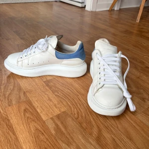 Oversized Alexander McQueen sneakers - Vita sneakers från Alexander McQueen. Blå mockadetalj och silvertryckt logotyp vid hälen.  Finns mindre skavanker, se bilder. Skosnören är nya, men skickar även med de gamla.  Sulhöjd: 3,5 cm.