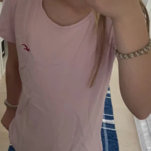 Ljusrosa t-shirt från Hollister - Säljer en ljusrosa t-shirt från Hollister med liten röd logga på bröstet. Modellen är 12 år och 153cm