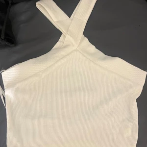 Vit croppad linnetopp - Snygg vit croppad linnetopp med ribbad struktur och korsade axelband. Perfekt för varma dagar eller som ett lager under en skjorta. Enkel och stilren design som passar till mycket.