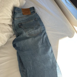 Levis 501 ljusblå jeans - Klassiska Levis 501 jeans i ljusblå tvätt med raka ben och femficksmodell. Jeansen har knappgylf och den ikoniska Levis-lappen bak i midjan. Perfekta för en avslappnad och tidlös stil.