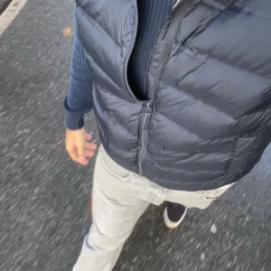 Svart dunväst med dragkedja - Snygg svart dunväst med dragkedja framtill. Perfekt att bära över en tröja för extra värme under kyliga dagar. Västen har en klassisk passform och är enkel att matcha med olika outfits. Säljer den då den inte används.