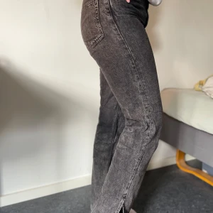 Svarta jeans med slits  - Säljer ett par svarta straight jeans med slits från Grunt med hög midja. Jeansen har en lätt tvättad look och upplevs mörkgrå. De har klassiska fickor både fram och bak. Perfekta för dig som gillar en tidlös och trendig stil.