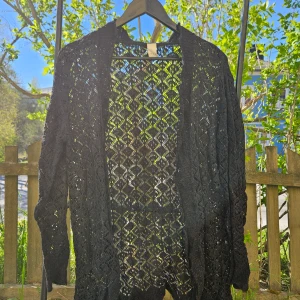 Svart spetskofta - Säljer en svart kofta med spetsdetaljer och genombrutet mönster. Perfekt att slänga över en topp för en snygg lager-på-lager-look. Koftan har lång ärm och är öppen framtill.