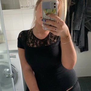 Svart topp med spets från H&M - Säljer en svart topp från H&M med korta ärmar och vacker spets upptill över axlar och bröst. Toppen har rund halsringning och är figurnära i modellen. Perfekt att styla till olika outfits!