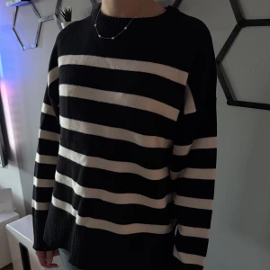 Svartvit randig stickad tröja - Säljer en svart och vit randig stickad tröja med rund hals. Tröjan har en avslappnad passform och långa ärmar. Perfekt för dig som gillar klassiska mönster och vill ha något bekvämt och stilrent.