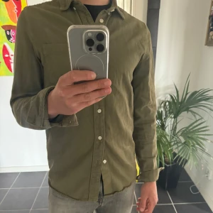 Olivgrön skjorta från Zara - Säljer en olivgrön skjorta/overshirt från Zara med klassisk krage och knäppning framtill. Skjortan har en bröstficka och är långärmad, perfekt för en stilren och avslappnad look. Overshirten är inprincip aldrig använd skicket är som nytt hör av er för eventulla frågor!!