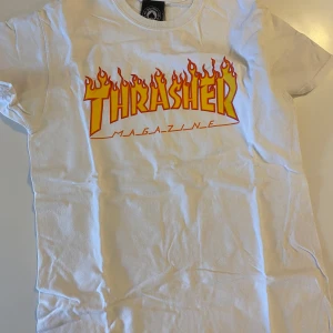 Vit Thrasher t-shirt  - Vit t-shirt från Thrasher med den klassiska flames-loggan i gult och rött på bröstet. 