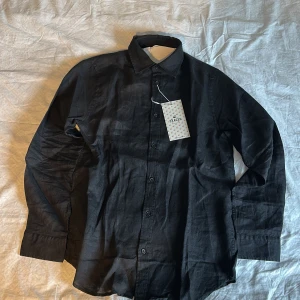 Svart linneskjorta från Skagen Clothing - Helt ny! Aldrig använd. Snygg svart skjorta i linne från Skagen. Klassisk krage, knäppning framtill och långa ärmar med dubbla knappar vid manschetten. Perfekt för en stilren look och enkel att matcha med olika outfits. Nypris 1100kr